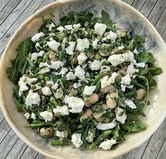 a white bowl filled with greens and feta cheese on top of a wooden table