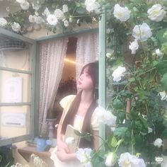 a woman sitting in front of a window next to white flowers and greenery on the outside