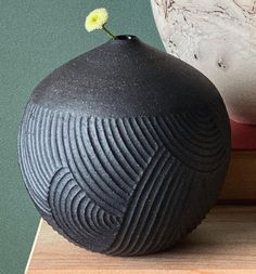 a black vase sitting on top of a wooden table next to a white vase with a yellow flower in it