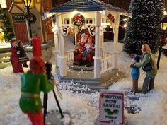 miniature christmas decorations in front of a small gazebo with people on it and trees