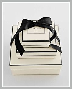 three white boxes with black ribbon tied around the top and one has a bow on it