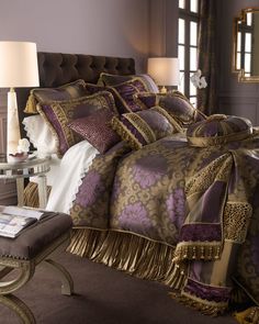 a large bed with purple and gold comforters in a room next to a window