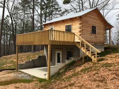 a wooden cabin with stairs leading up to the front door and second story on top of a hill