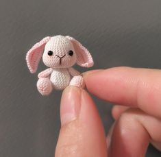 a tiny white stuffed animal sitting on top of someone's finger