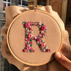 someone is holding up an embroidered letter in front of their face and the letters are made out of flowers