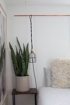 a bedroom with a bed and a plant on the nightstand next to it, in front of a white wall