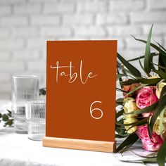 a table number with flowers and candles on the table in front of it is an orange sign that says table 6