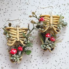 two pairs of earrings made out of bones and mushrooms, with plants growing from them