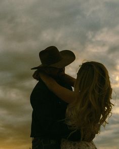 a man and woman standing next to each other under a cloudy sky with the sun setting behind them