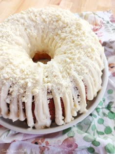 a bundt cake with white icing sitting on a floral cloth covered tablecloth