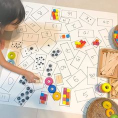 a young child playing with wooden toys on the floor in front of a large sheet of paper