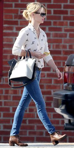 a woman walking down the street carrying a white handbag and wearing blue denims