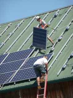 two men working on the roof of a building with solar panels and ladders attached to it