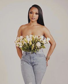 a woman with flowers in her hand and jeans on, posing for the camera while wearing high heels