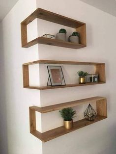 three wooden shelves on the wall with plants and candles in them, one is empty