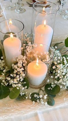 candles are lit on a table with flowers and greenery