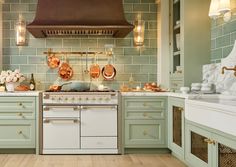 a kitchen with green cabinets and copper accessories on the stove top, along with white counter tops