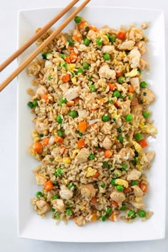 rice with chicken and vegetables on a white plate next to chopsticks