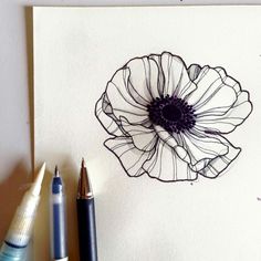 a drawing of a flower on paper next to some pens