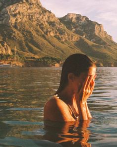 a woman is floating in the water with her hands to her face and looking off into the distance