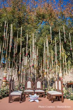 an outdoor wedding setup with chairs and flowers hanging from the ceiling, surrounded by greenery