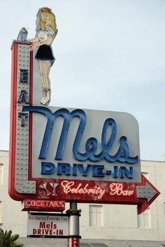 the neon sign for mel's drive - in is lit up and has a woman on it