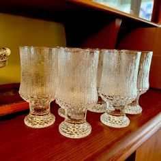 four glasses sitting on top of a wooden table next to a mirror in a room