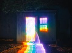 a rainbow colored bench in front of a building with two windows on the side and one door open