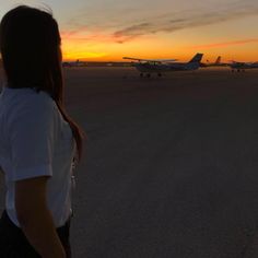 a woman standing on an airport tarmac looking at the planes in the distance as the sun sets