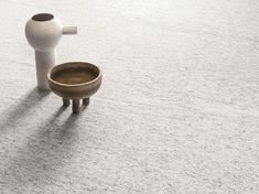 a white vase sitting on top of a cement floor next to a wooden cup holder