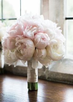 a bridal bouquet on a wooden table in front of a window with white and pink peonies