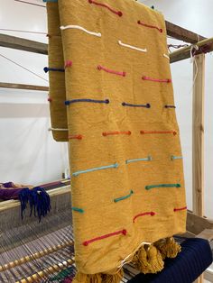 a yellow blanket is hanging on an old weaving loom with colorful thread and tassels