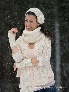 a woman wearing a white knitted hat and scarf in the snow with her arms crossed