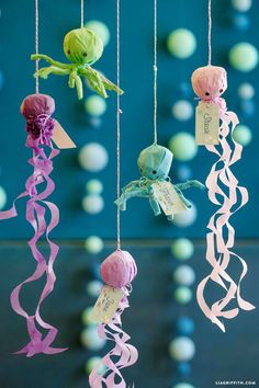 an assortment of paper flowers hanging from strings in front of a blue background with white and green balls