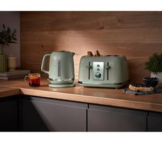 two green toasters sitting on top of a counter next to a cup of tea