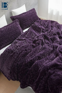 a bed covered in purple fluffy blankets and pillows