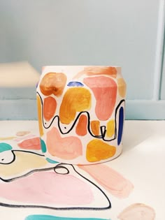 a cup sitting on top of a white table next to a painting covered jar with the word love