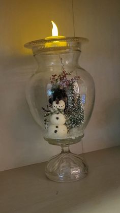 a snowman in a glass vase with a lit candle