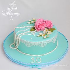 a blue cake with white lace and pink flowers on top, sitting on a plate