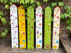 three colorful wooden rulers are lined up against a brick wall with plants in the background