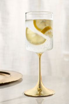 a glass filled with liquid and lemon slices on top of a table next to a plate