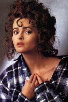 a woman with curly hair wearing a checkered shirt and holding her hands on her chest