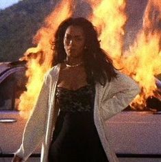 a woman standing in front of a car with fire coming out of the back window