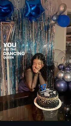 a woman sitting at a table with a cake in front of her and balloons behind her