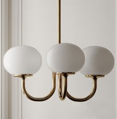 three lights hanging from a brass chandelier with white glass balls on the arms