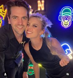 a man and woman posing for a photo in front of neon signs