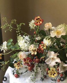 a vase filled with lots of flowers on top of a white tablecloth covered table