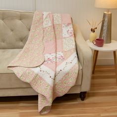 a couch with a pink and white quilt on it next to a table with a lamp