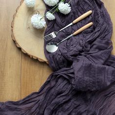 flowers and utensils are laid out on a wooden board with purple fabric draped over it