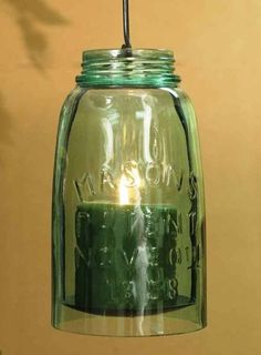 a green mason jar with a lit candle in the center hanging from a ceiling fixture